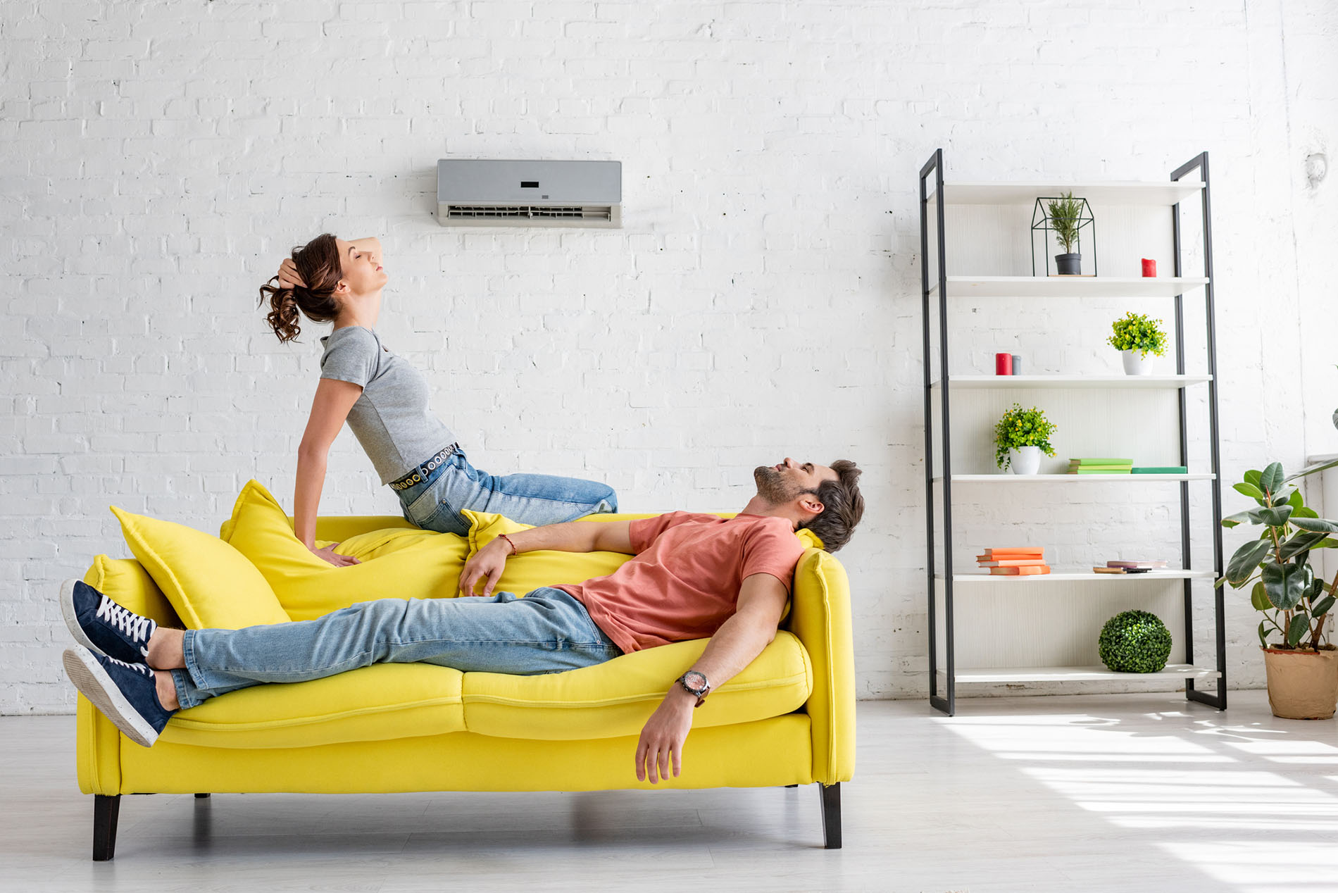 young man and woman resting on yellow sofa under ductless air conditioner at home